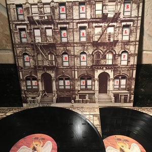 May include: Led Zeppelin's "Physical Graffiti" album cover featuring a brownstone building with the album title and band name. Two vinyl records are visible, showcasing the album's label art with an angel illustration.