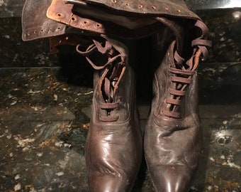 May include: A pair of brown leather boots with laces and pointed toes. The boots have a decorative stitching detail around the top of the boot.