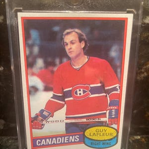 Puede incluir: Tarjeta de hockey de Guy Lafleur con la camiseta roja de los Canadiens de Montreal con rayas azules y blancas. La tarjeta está en un soporte protector. Se ve el texto "CANADIENS" y "RIGHT WING".