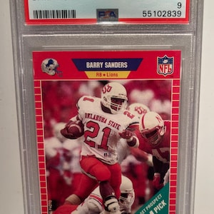 May include: A 1989 Pro Set Barry Sanders football card, graded as Mint 9. The card features a photo of Sanders in an Oklahoma State uniform, number 21, running with the ball. The card is encased in a protective holder.