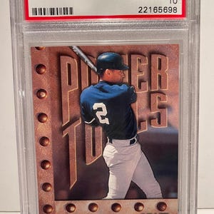 May include: A baseball trading card featuring Derek Jeter in a New York Yankees uniform. The card is encased in a protective holder and includes the text "1998 LEAF R & S DEREK JETER" and "POWER TOOLS". The card is graded GEM MT 10.