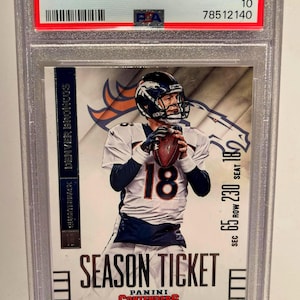 May include: A 2014 Panini Contenders Peyton Manning football card, graded GEM MT 10, encased in a protective holder. The card features Manning in his Denver Broncos uniform, holding a football. The card's text includes "Season Ticket" and "Quarterback".