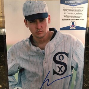 May include: A framed photo of a baseball player wearing a white and blue striped jersey with the letters "SOX" on the front. The player is wearing a blue and white striped baseball cap and has a blue signature on the jersey. The photo has a Beckett Certificate of Authenticity with the serial number 104538.