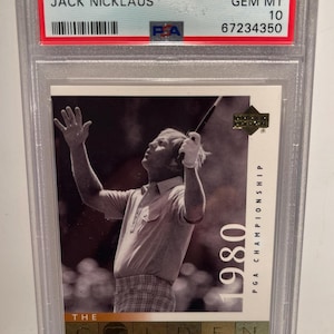 Puede incluir: Una tarjeta coleccionable de golf Upper Deck 2001 calificada con Jack Nicklaus. La tarjeta muestra a Nicklaus en acción, con el texto "2001 Upper Deck Golf Jack Nicklaus" en la parte superior. La tarjeta está dentro de un soporte protector.