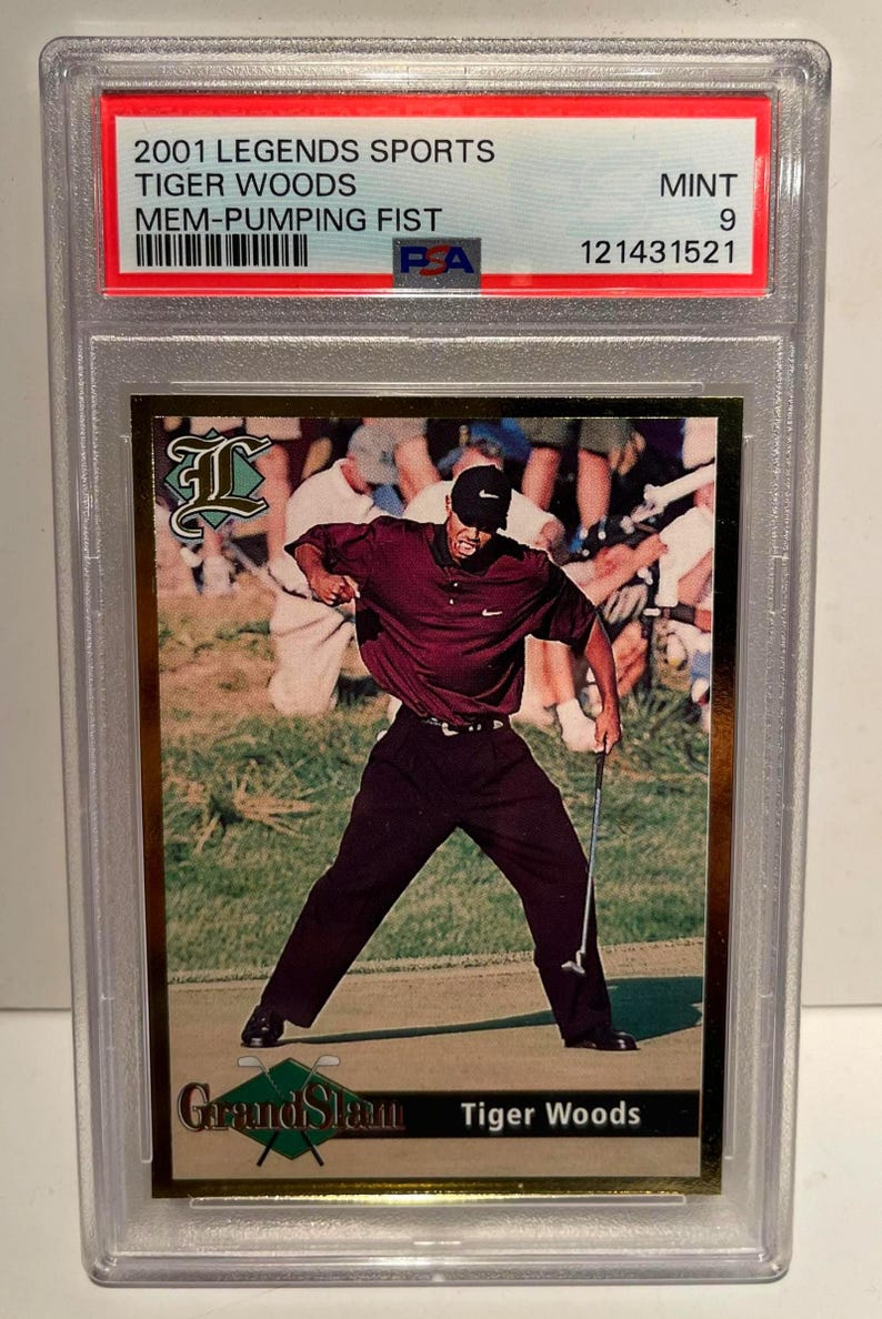 Puede incluir: Una tarjeta de intercambio deportiva calificada con Tiger Woods. La tarjeta muestra a Woods con una camisa burdeos y pantalones negros, a mitad de swing. La tarjeta est&aacute; etiquetada como "2001 Legends Sports" y "Mem-Pumping Fist."