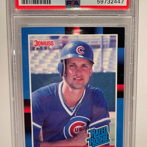 May include: A 1988 Donruss Mark Grace baseball card, graded GEM MT 10 by PSA. The card features a portrait of Mark Grace in a Chicago Cubs uniform. The card is encased in a protective plastic holder.