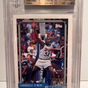May include: A graded Shaquille O'Neal basketball card from the 1992-93 Topps set, featuring O'Neal in his Orlando Magic uniform. The card is encased in a protective holder with a Beckett grading label, displaying a 9.5 grade.