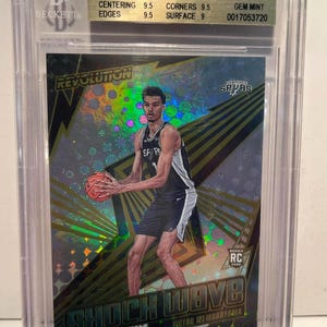 Op de afbeelding: Een beoordeelde Panini Revolution Shock Wave basketbalkaart met Victor Wembanyama in een San Antonio Spurs-uniform. De kaart zit in een beschermende houder met een Beckett-beoordeling van 9,5. De kaart heeft een holografisch ontwerp.