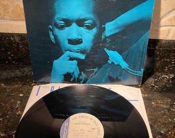 Può includere: Un disco in vinile nero con un'etichetta blu. L'etichetta presenta il testo "The Finest in Jazz Since 1939" e "Blue Note" con un logo di nota blu stilizzato. Il disco è intitolato "Blue Train" di John Coltrane.