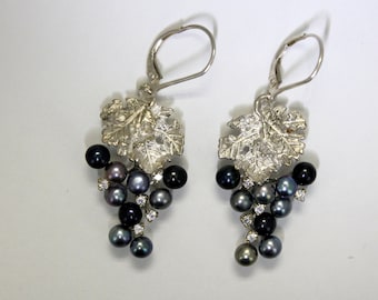 May include: Silver earrings with a grapevine design and black pearls. The earrings feature a leaf design with a cluster of black pearls hanging from the leaves.