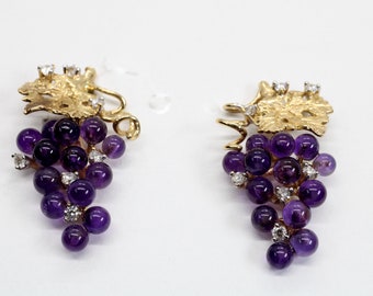 May include: A pair of gold earrings featuring a grape cluster design with amethyst and diamond accents.