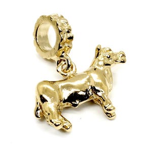 May include: A gold-colored charm in the shape of a bull. The charm has a detailed design, with visible legs, a tail, and a head. The charm has a loop at the top for attaching to a bracelet or necklace. The bull is facing to the right.