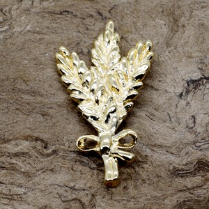 May include: A gold-coloured metal pin shaped like a sprig of wheat tied with a bow.