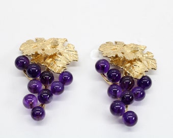 May include: A pair of gold earrings with purple amethyst stones shaped like grapes hanging from gold leaves.
