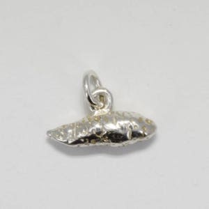 May include: A silver charm in the shape of a sweet potato. The charm has a textured surface and a loop for attaching to a bracelet or necklace.