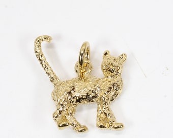 May include: A gold-colored charm in the shape of a cat. The cat is standing on all four paws with its tail curled up behind it. The charm has a textured surface.