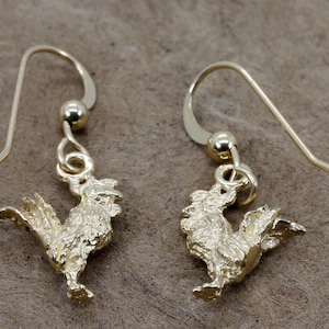May include: A pair of gold-tone rooster earrings with a textured finish. The earrings have a simple hook fastening.