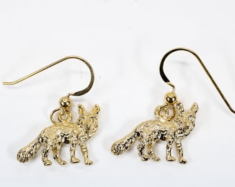Op de afbeelding: Een paar gouden oorbellen met een vos-hanger. De vossen zijn gedetailleerd en hebben een textuur.