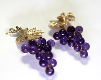 May include: A pair of gold earrings with amethyst grape clusters. Each earring features a small gold leaf design.