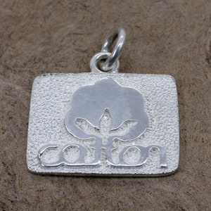 May include: Silver charm with a cotton boll design and the word "cotton" engraved on it.