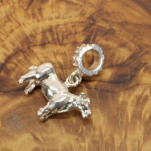 May include: A silver-colored charm in the shape of a horse, with a detailed design. The charm has a loop at the top for attaching to a bracelet or necklace. The horse is depicted in a running pose.