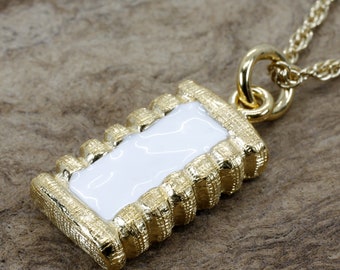 Puede incluir: Un collar de cadena de oro con un colgante de esmalte blanco. El colgante es rectangular y tiene un borde de oro texturizado.