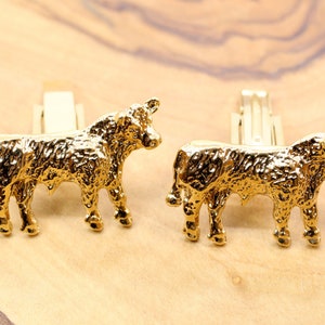 May include: A pair of gold-tone cufflinks featuring a detailed, textured design of a bull. The cufflinks are a classic and stylish accessory for any man.