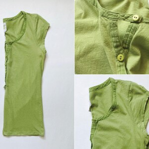 May include: A light green, short-sleeved shirt with a button-up neckline. The shirt has a textured appearance and a relaxed fit. The design includes a small, decorative detail on the side. The fabric appears to be a soft, breathable material.