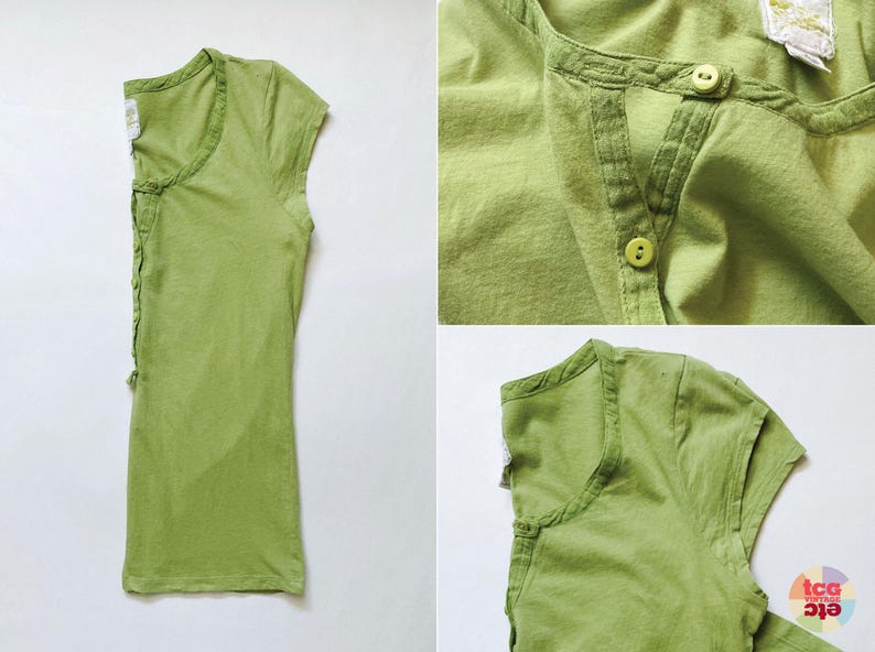 May include: A light green, short-sleeved shirt with a button-up neckline. The shirt has a textured appearance and a relaxed fit. The design includes a small, decorative detail on the side. The fabric appears to be a soft, breathable material.