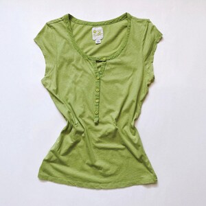 May include: A light green, short-sleeved shirt with a scoop neck and a button-down placket. The shirt has a slightly faded appearance and a small tag near the neckline. The shirt is made of a soft, lightweight fabric.