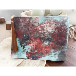 Könnte beinhalten: Eine blaue und rote Clutch mit abstraktem Druck, einem braunen Lederriemen und einem Reißverschluss.