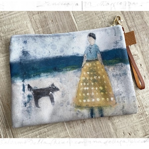Könnte beinhalten: Leinwand-Clutch mit einer künstlerischen Illustration einer Person, eines Hundes und einer Landschaft. Die Person trägt ein blaues Hemd und einen gelben Rock mit weißen Punkten. Die Clutch hat eine braune Leder-Handschlaufe und einen goldfarbenen Reißverschluss.