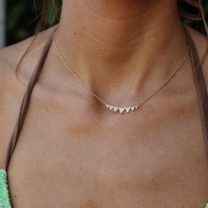 Puede incluir: Un collar de oro con una cadena delicada y una fila de pequeños colgantes en forma de triángulo engastados con pequeños diamantes.