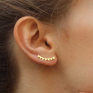 Puede incluir: Primer plano de la oreja de una persona con un pendiente de aro dorado con una fila de pequeñas formas triangulares.