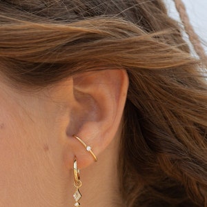 Arc-shaped earring with zircon in the center, held as if it were a staple, in 925 sterling silver and 24k gold plated