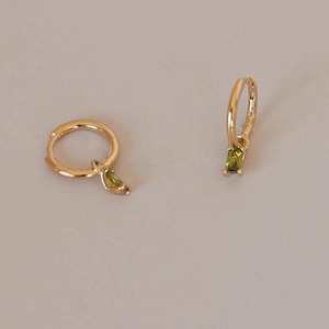 Puede incluir: Un par de pendientes de aro de oro con una pequeña piedra preciosa verde que cuelga de cada aro.