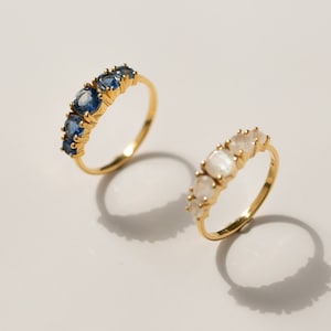 May include: Two gold rings with gemstones. The ring on the left has blue gemstones and the ring on the right has white gemstones.