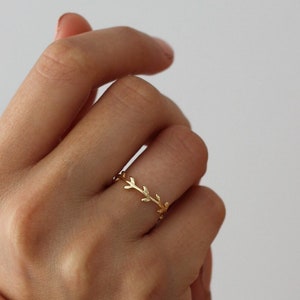 Könnte beinhalten: Ein goldener Ring mit einem zarten Zweigdesign. Der Ring wird an einem Finger getragen.