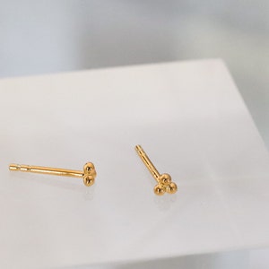 May include: Two pairs of gold stud earrings. One pair has two small gold balls, the other pair has three small gold balls.