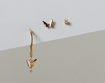 以下が含まれることがあります： 金の蝶のイヤリングのセット。片方のイヤリングは、蝶のチャームがぶら下がったフープで、もう片方は小さな蝶のスタッドです。