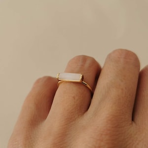 Può includere: Anello dorato con pietra rettangolare colorata. La fascia e l'incastonatura dell'anello sono dorate. La pietra è disposta orizzontalmente. Design minimalista.