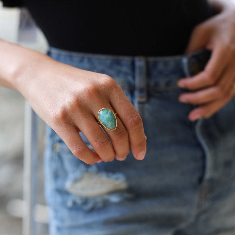 May include: A gold ring featuring a large, oval-shaped, light green gemstone.