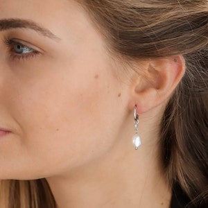 Long hoop earrings with an irregularly shaped cultured freshwater pearl pendant in gold on sterling silver