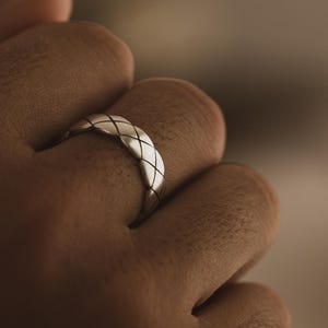 Könnte beinhalten: Ein silberner Ring mit einem geflochtenen Muster. Der Ring befindet sich an einem Finger.