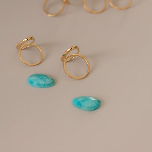 May include: Two gold rings with a delicate design, stacked on top of each other. Two teal green gemstones are also pictured.