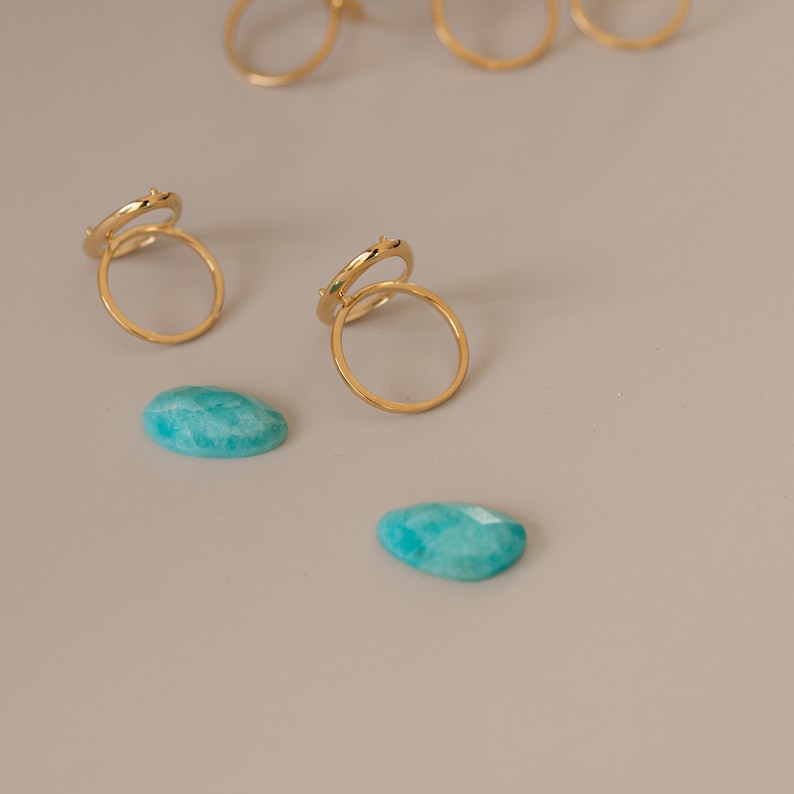 May include: Two gold rings with a delicate design, stacked on top of each other. Two teal green gemstones are also pictured.