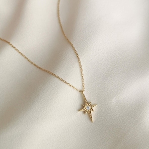 Puede incluir: Un collar de oro con un colgante en forma de estrella con una peque&ntilde;a piedra transparente en el centro.
