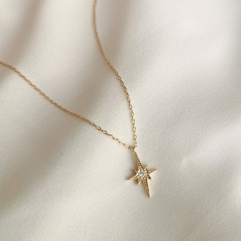 Puede incluir: Un collar de oro con un colgante en forma de estrella con una peque&ntilde;a piedra transparente en el centro.