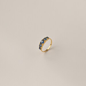 May include: A gold ring with a row of blue oval-shaped gemstones.