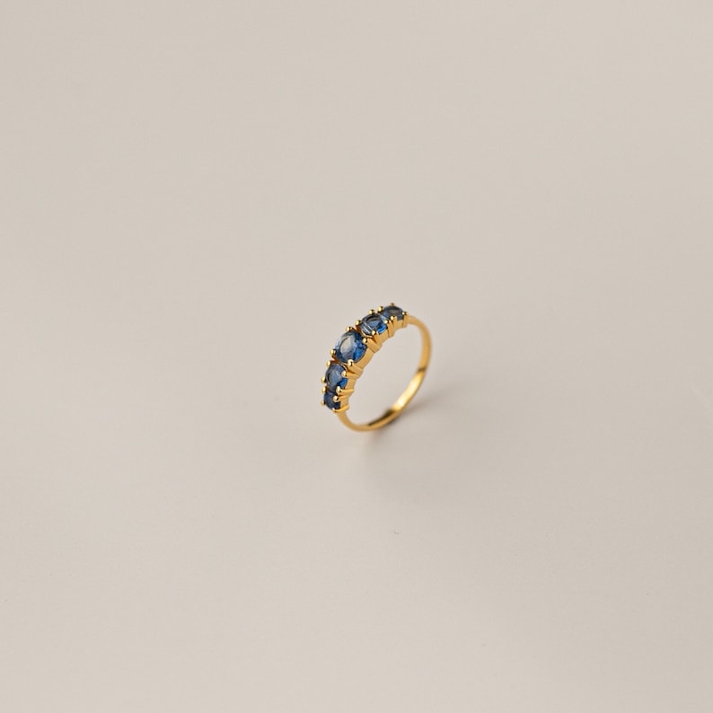 May include: A gold ring with a row of blue oval-shaped gemstones.